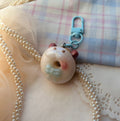 Donut-shaped Poro keychain with a bow on a textured fabric background
